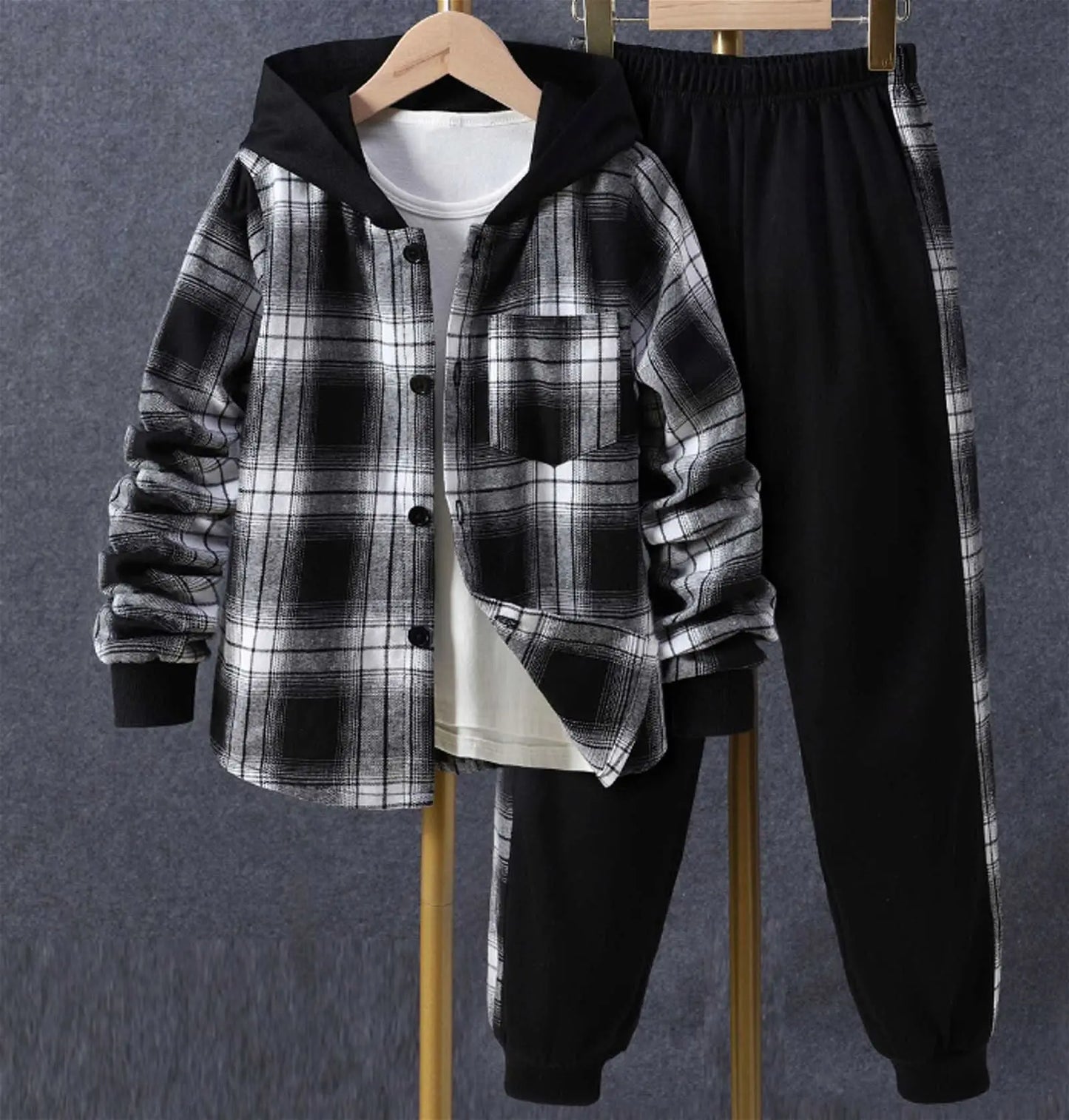 A Reign + Sun toddler boy plaid outfit hangs on hangers—a black and white hooded shirt jacket over a white shirt with black elastic-waist pants—perfect for baby boys’ spring/autumn, displayed against a gray background.