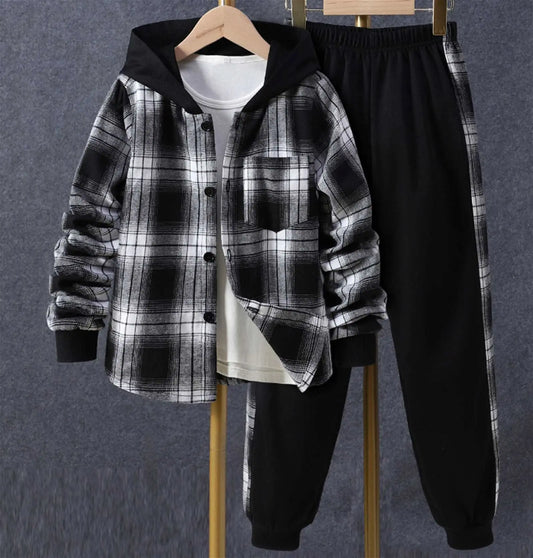 A Reign + Sun toddler boy plaid outfit hangs on hangers—a black and white hooded shirt jacket over a white shirt with black elastic-waist pants—perfect for baby boys’ spring/autumn, displayed against a gray background.